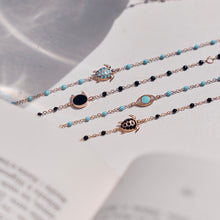 Photo de plusieurs bracelets Gigi Clozeau, aux couleurs noire et turquoise, disposés sur une table.