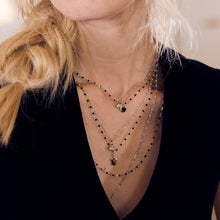 Photo du cou d’une femme portant différents colliers Gigi Clozeau aux couleurs turquoise et noires.