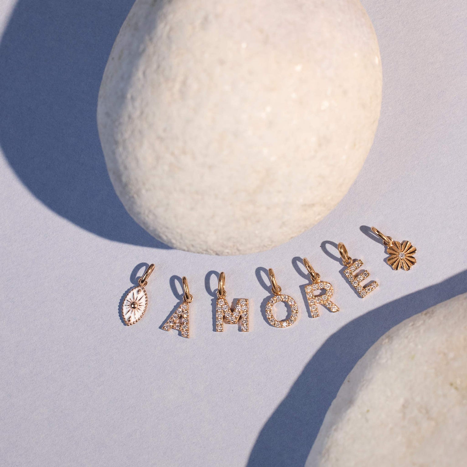 Photo de nature morte de plusieurs pendentifs Lucky Letters posés, formant le mot « Amore », accompagnés d’autres pendentifs Gigi Clozeau.