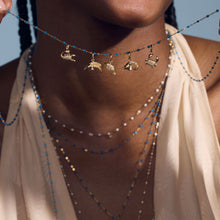 Photo de plusieurs pendentifs zodiaque suspendus sur un collier au décolleté d’une femme.